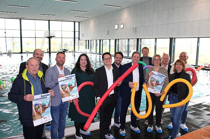 Gruppenbild vieler Menschen in einem Schwimmbad, einige halten Poolnudeln und Plakate in der Hand.