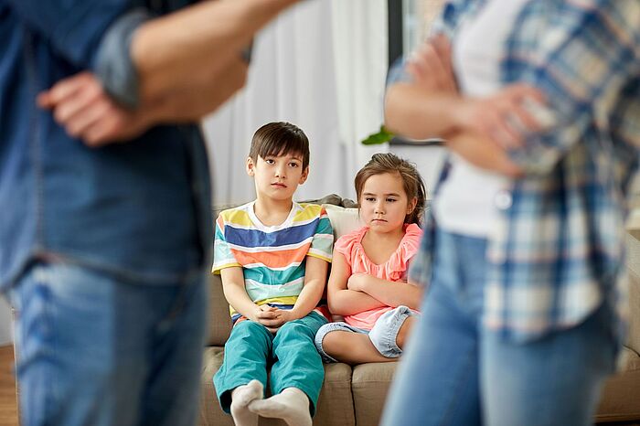 Ein Junge und ein Mädchen auf dem Sofa schauen bedrückt Erwachsenen beim streiten zu