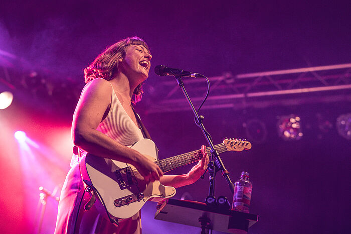 Das Foto zeigt die Sängerin Teresa Bergman beim Singen und Gitarrespielen auf der Bühne