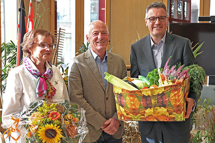 Eine Frau und zwei Männer halten einen Strauß Sonnenblumen und eine herbstlich geschmückte Kiste.