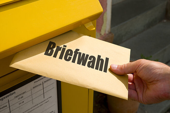 Hand wirft Umschlag mit Briefwahlunterlagen in öffentlichen Briefkasten