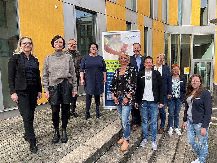 10 Personen stehen draußen vor einem Banner.