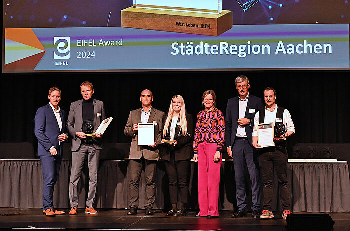 Die städteregionalen Gewinnerteams des Eifelawards stehen auf einer Bühne. Dezernent Markus Terodde überreicht den Award.